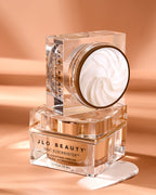 JLO Beauty That Blockbuster Hydrating Cream in a clear glass jar with a gold-toned lid.