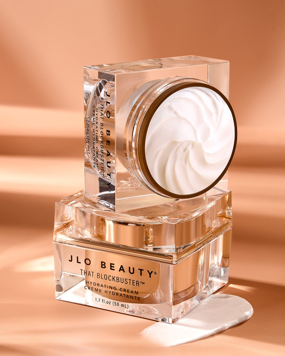 JLO Beauty That Blockbuster Hydrating Cream in a clear glass jar with a gold-toned lid.