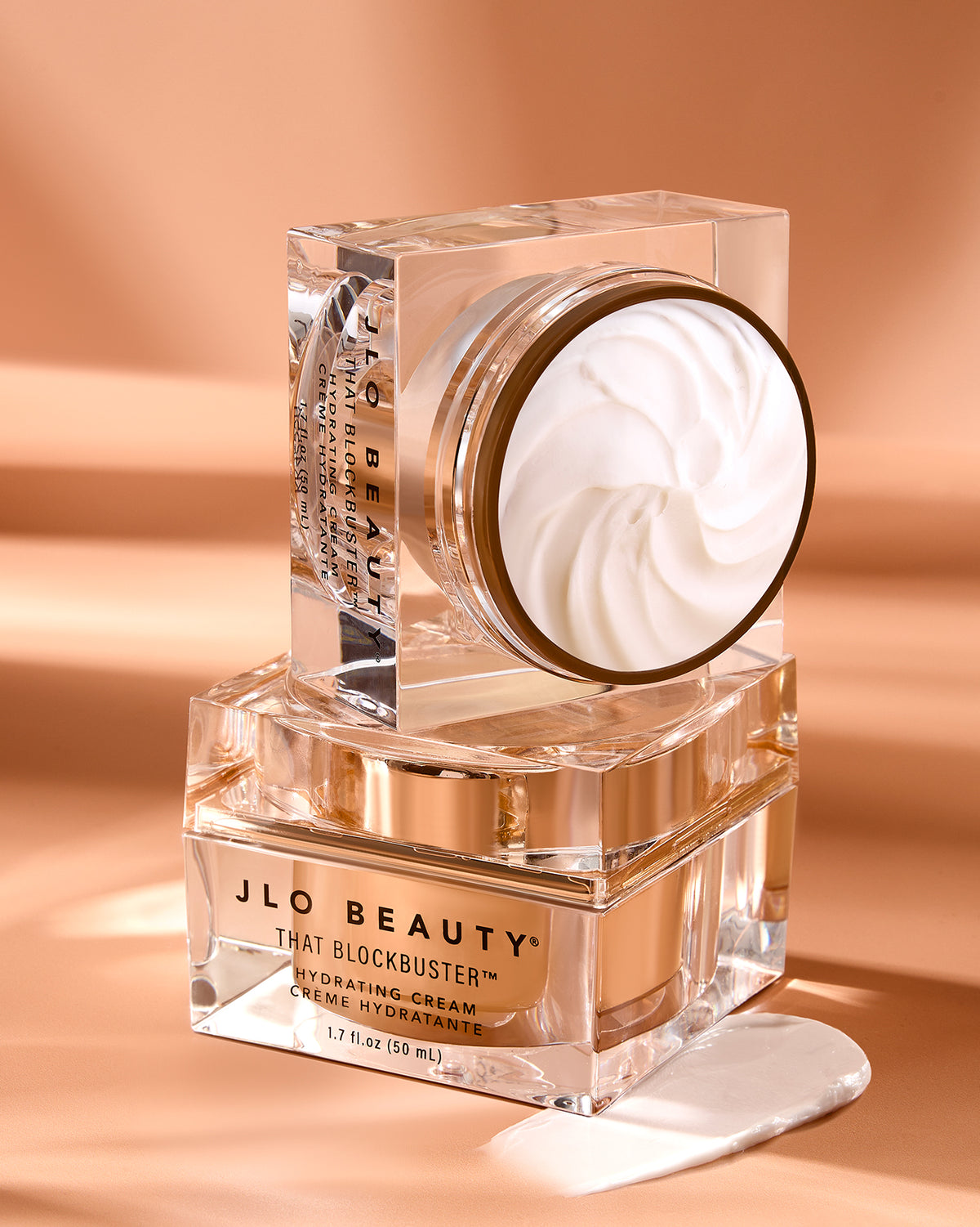 Two square jars of JLo Beauty That Blockbuster Hydration cream 50ml stacked on top of each other with rose colour background.
