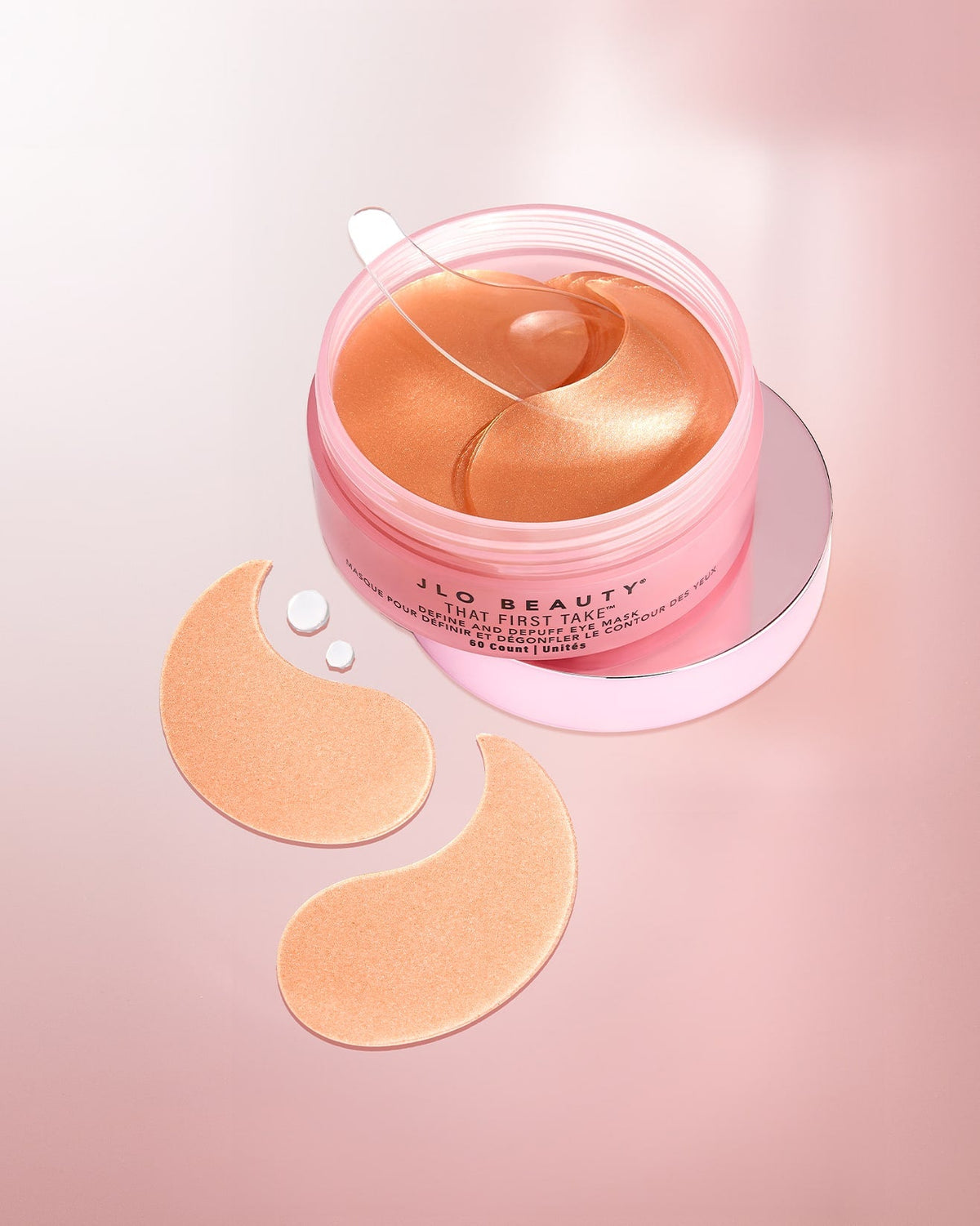JLO Beauty Eye Masks in a pink jar with a clear lid, shown with two peach-colored eye patches 
