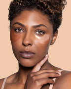 A close-up portrait of a woman with JLO Beauty eye patches under her eyes and on her cheeks