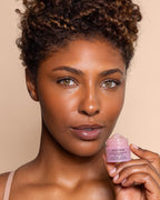 A close-up of a woman holding a small pink jar of Beso Balm.