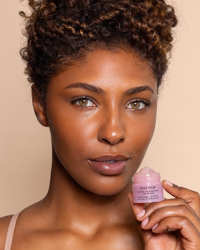A close-up of a woman holding a small pink jar of Beso Balm.