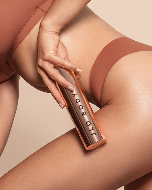 Model applying JLO Beauty Body Serum to her leg.