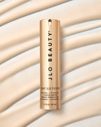 A gold cylindrical bottle of JLO Beauty That JLO Fusion Retinal + Vitamin C Power Serum, set against cream liquid textures.