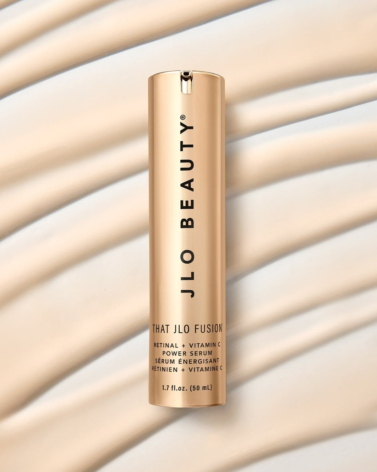 A gold cylindrical bottle of JLO Beauty That JLO Fusion Retinal + Vitamin C Power Serum, set against cream liquid textures.