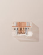 JLO Beauty That Blockbuster Hydrating cream jar on a beige background