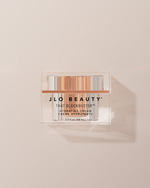 JLO Beauty That Blockbuster Hydrating cream jar on a beige background