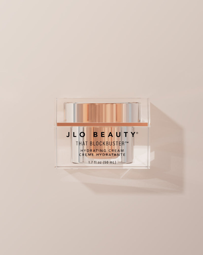 JLO Beauty That Blockbuster Hydrating cream jar on a beige background