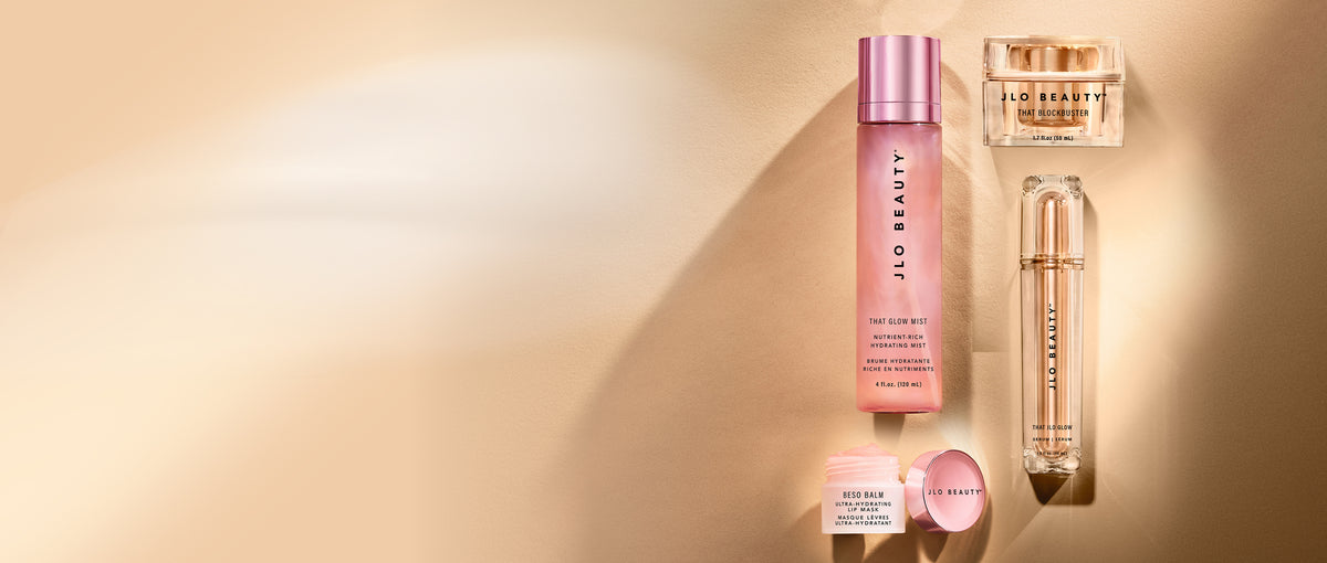 A collection of JLO Beauty skincare products arranged on a warm beige background with soft shadows.
